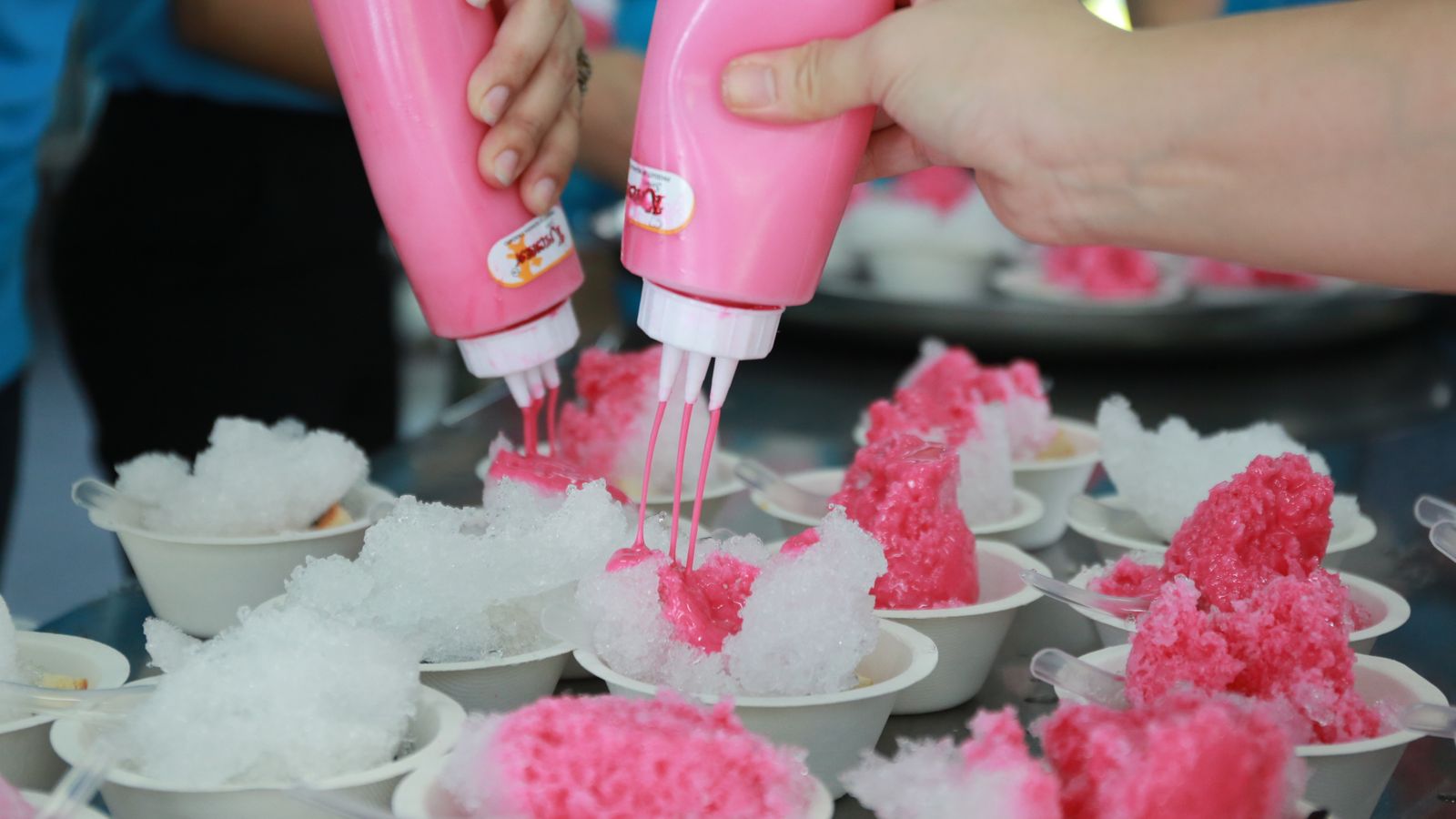 Syrup being poured over cups of shave ice